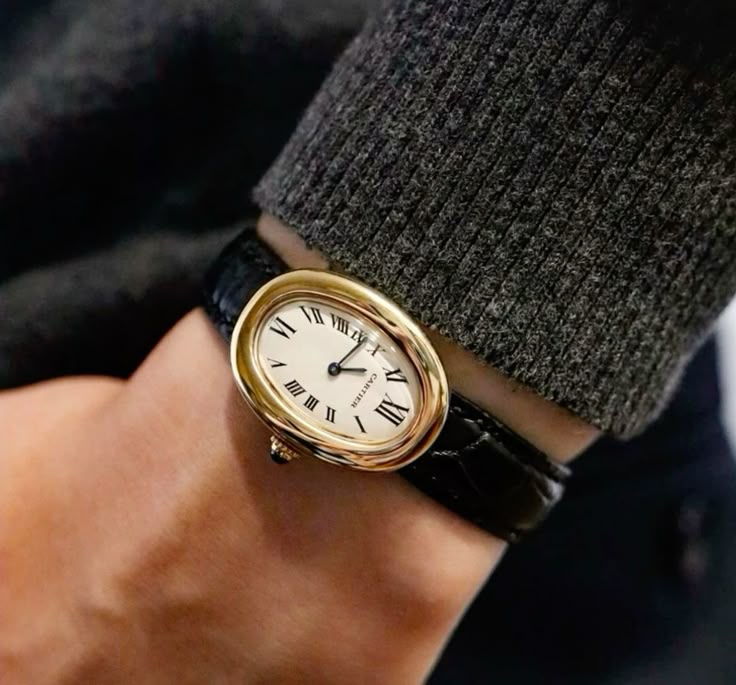 Montre ovale de teinte dorée portée avec une manche grise