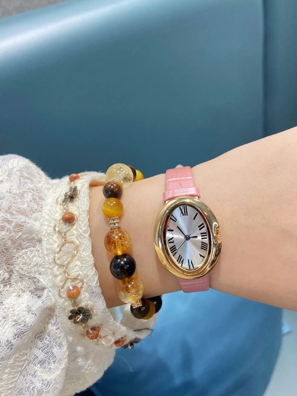 Montre ovale de teinte dorée à bracelet rose présentée dans un coffret