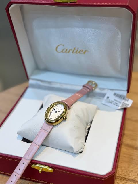 Montre à bracelet rose disposée sur un coussin dans un coffret ouvert